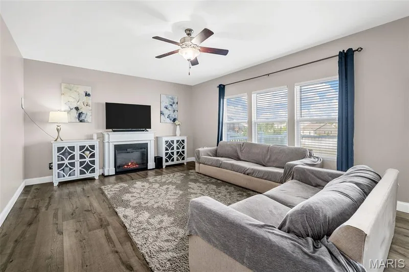 Spacious living area featuring wood-finish flooring, a ceiling fan, and multiple windows providing natural light — 543 Country Chase Drive, Lake St. Louis, MO 63367