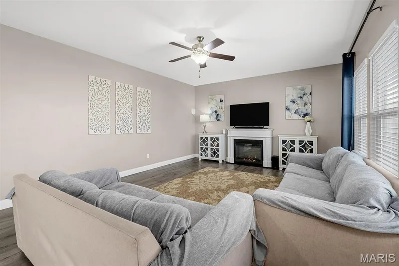 Living area with wood-finish flooring, a ceiling fan, and a fireplace with a white mantel — 543 Country Chase Drive, Lake St. Louis, MO 63367
