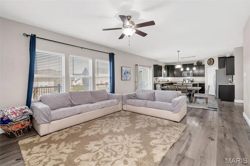 Open-concept living area featuring wood-finish flooring, a ceiling fan, and large windows with blinds — 543 Country Chase Drive, Lake St. Louis, MO 63367