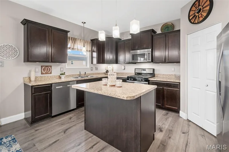 Kitchen featuring dark wood cabinetry, light-toned countertops, stainless steel appliances, a central island, and wood-finish flooring — 543 Country Chase Drive, Lake St. Louis, MO 63367