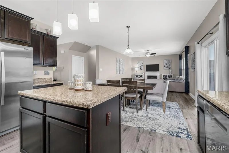 Open-concept living area featuring wood-finish flooring, a kitchen island with stone-finish countertop, stainless steel appliances, and dark wood cabinetry — 543 Country Chase Drive, Lake St. Louis, MO 63367