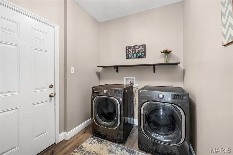 Dedicated laundry space featuring wood-finish flooring, a white paneled door, and a wall-mounted shelf — 543 Country Chase Drive, Lake St. Louis, MO 63367