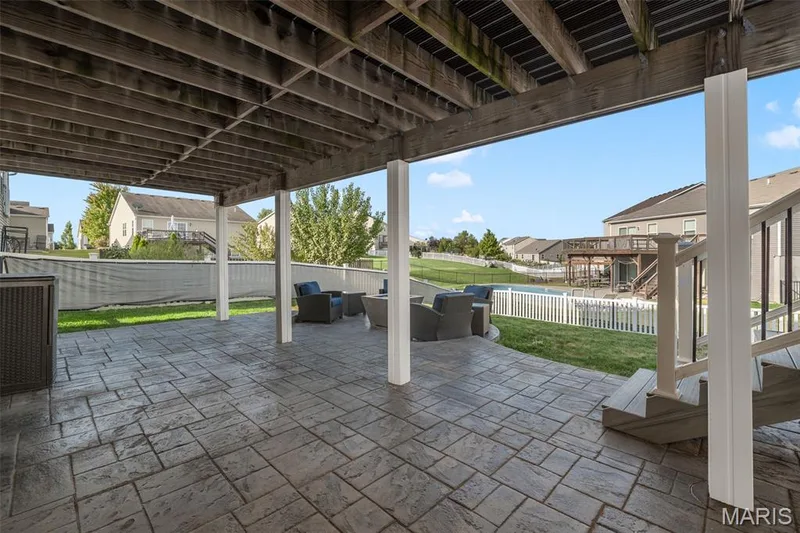 Expansive stamped concrete patio with overhead wood-beam deck structure and white support columns — 543 Country Chase Drive, Lake St. Louis, MO 63367
