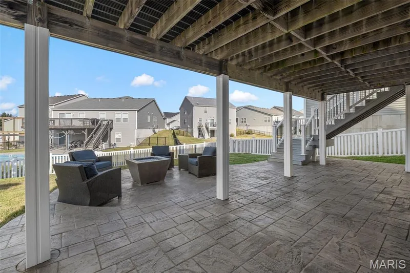 Expansive covered stamped concrete patio with sturdy support columns, integrated staircase, and white picket fencing — 543 Country Chase Drive, Lake St. Louis, MO 63367