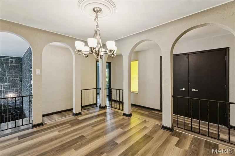 Wood-finish flooring throughout, multiple arched doorways, wrought iron railings, and a chandelier with a decorative ceiling medallion — 2801 Droste Road, St Charles, MO 63301