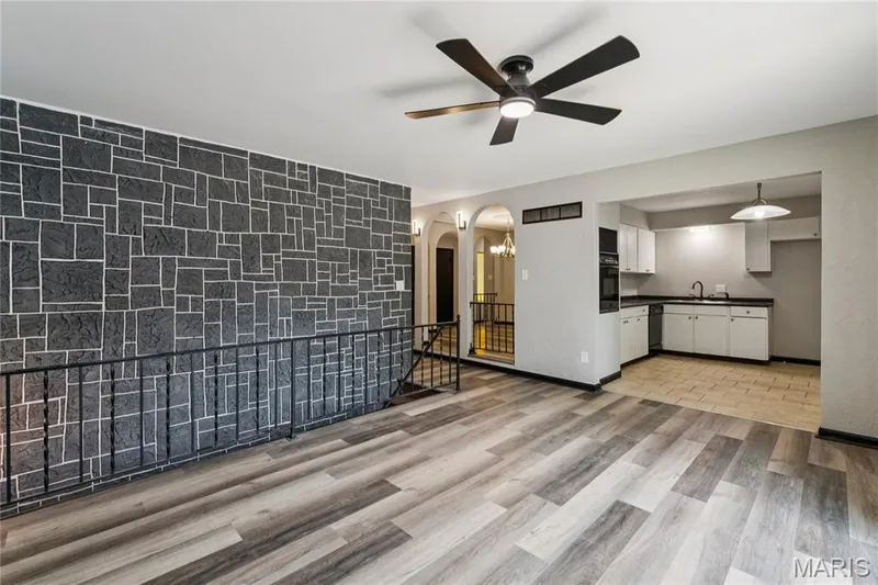 Feature stone wall, wood-finish flooring, ceiling fan, white cabinetry, and a black countertop — 2801 Droste Road, St Charles, MO 63301