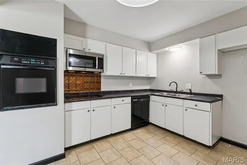 Kitchen featuring white cabinetry, dark countertops, a built-in oven, stainless steel microwave, and tiled flooring — 2801 Droste Road, St Charles, MO 63301
