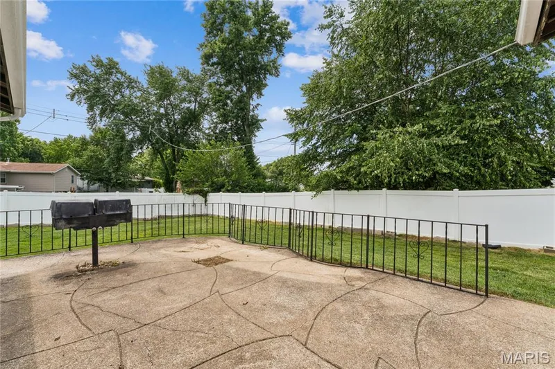 Concrete patio with decorative scoring, wrought iron fencing, a built-in grill, and a white privacy fence — 2801 Droste Road, St Charles, MO 63301
