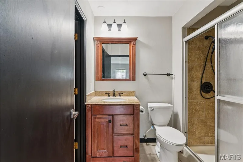 Wood-finish vanity with a light-toned countertop, framed mirror, and a three-light fixture — 2801 Droste Road, St Charles, MO 63301