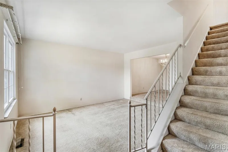 Entry foyer opens to expansive living area and desirable center stairway with neutral carpeting, large window, and staircase featuring metal railings — 1192 Cantina Drive, Chesterfield, MO 63141