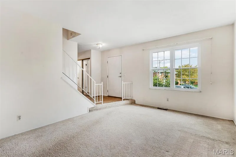 Carpeted living area with a double-hung window, white interior door, and staircase with metal railing — 1192 Cantina Drive, Chesterfield, MO 63141