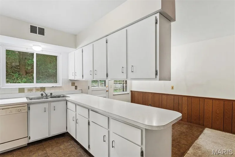 Loads of storage and counter space...White cabinetry, dual basin stainless steel sink, large window, wood-paneled wainscoting, and a breakfast bar — 1192 Cantina Drive, Chesterfield, MO 63141
