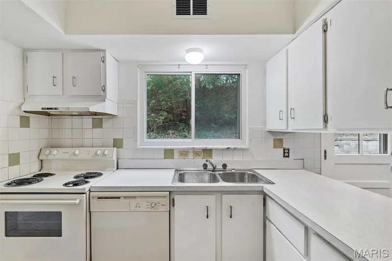 White cabinetry with ample storage, stainless steel double basin sink, and a decorative tile backsplash — 1192 Cantina Drive, Chesterfield, MO 63141