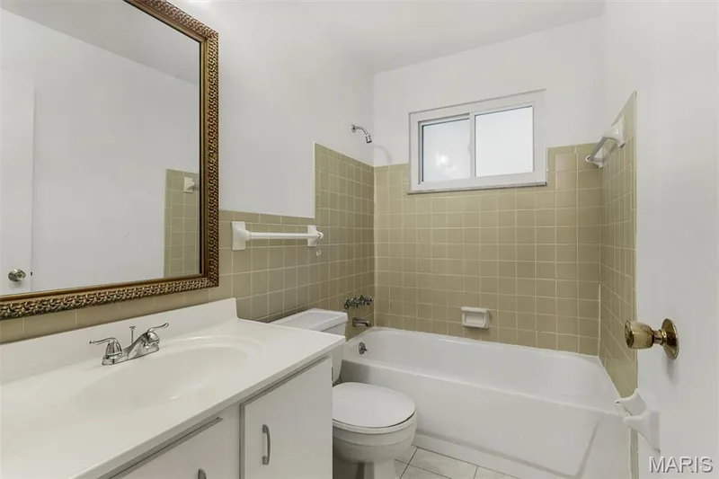 Hall bathroom has a large vanity with an integrated sink and base cabinetry, ceramic tile flooring, framed mirror, tiled bath enclosure, and a sliding window — 1192 Cantina Drive, Chesterfield, MO 63141