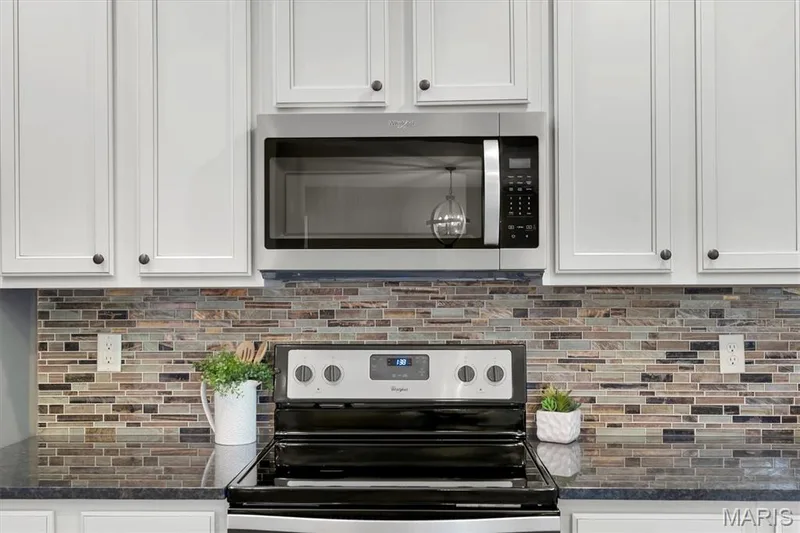 White shaker-style cabinetry with dark hardware, a stainless steel microwave, a glass cooktop range, a mosaic tile backsplash, and dark countertops — 56 Huntleigh Park Court, Wentzville, MO 63385