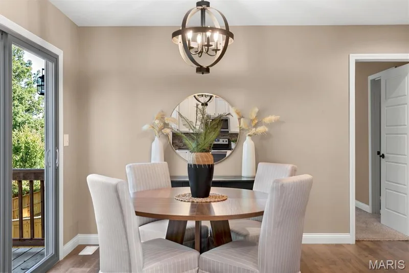 Dining area featuring wood-finish flooring, a contemporary chandelier, a sliding glass door to an exterior deck, and a rounded wood table — 56 Huntleigh Park Court, Wentzville, MO 63385