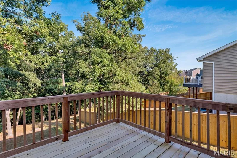 Expansive wood deck with a natural wood railing, surrounded by mature trees and a wood privacy fence — 56 Huntleigh Park Court, Wentzville, MO 63385