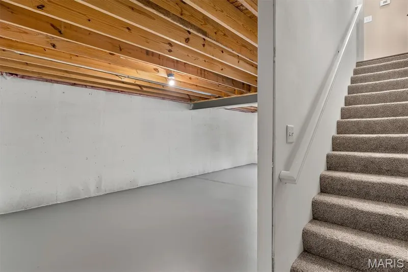 Unfinished basement space with exposed wood joists and concrete flooring, offering direct access to a carpeted staircase — 56 Huntleigh Park Court, Wentzville, MO 63385