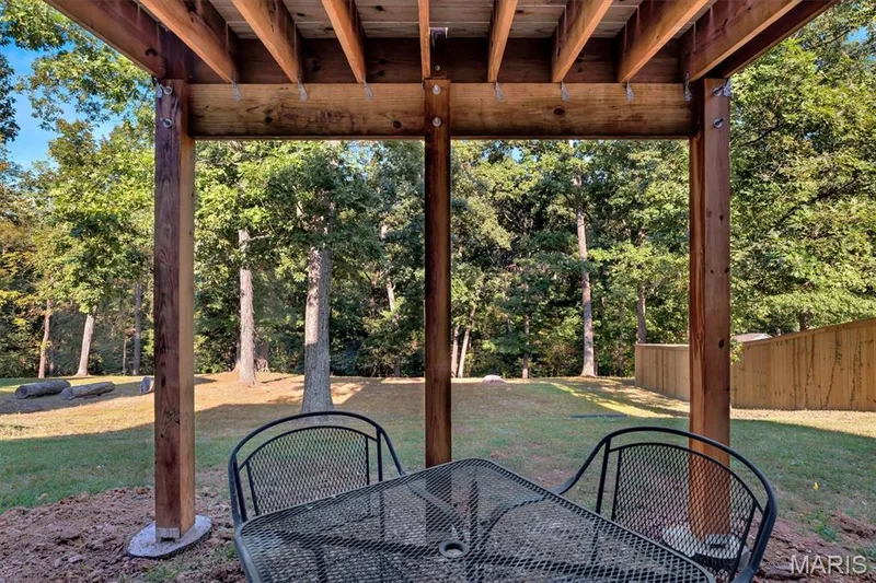 Covered patio with wood beam construction, overlooking a grassy yard with mature trees and wood fencing — 56 Huntleigh Park Court, Wentzville, MO 63385