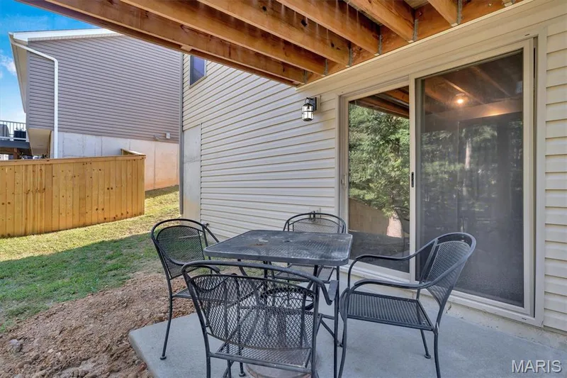 Concrete patio under a wood-beamed deck structure, featuring a sliding glass door with a screen — 56 Huntleigh Park Court, Wentzville, MO 63385