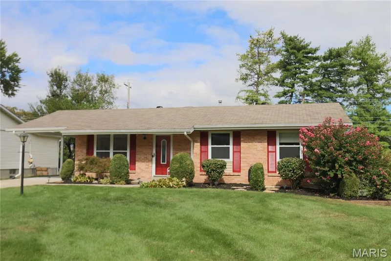 Side view of brick facade ranch home featuring a red entry door, decorative red shutters, a gabled roof, and established front landscaping — 3 Oxbow Road, St Peters, MO 63376