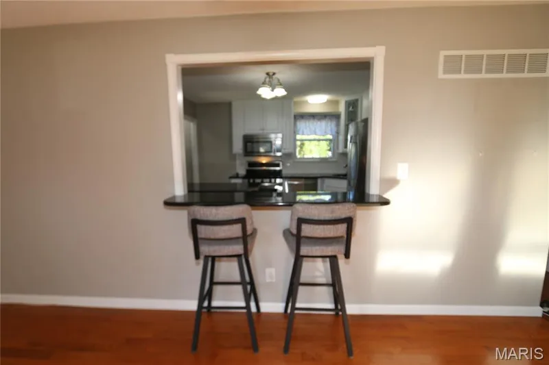 Pass-through opening from family room into kitchen with a black countertop and a wood floor. — 3 Oxbow Road, St Peters, MO 63376