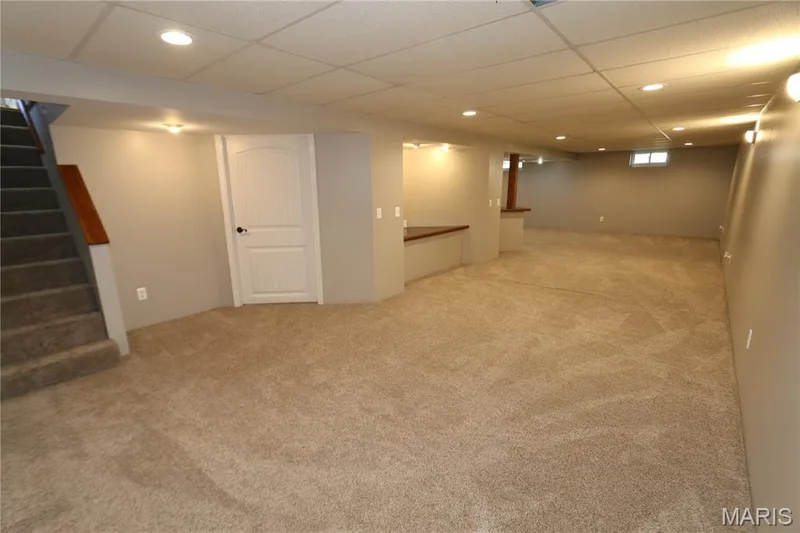 White door leads to the large laundry & storage area. Expansive carpeted area with recessed lighting, a built-in wood-finish counter, and a window for natural light — 3 Oxbow Road, St Peters, MO 63376