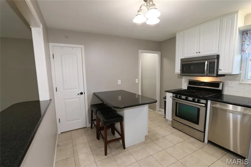 Doors closed. Kitchen featuring white cabinetry, stainless steel appliances, dark countertops, a subway tile backsplash, and light-toned floor tile — 3 Oxbow Road, St Peters, MO 63376