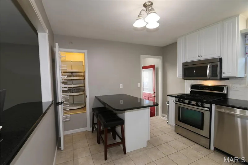 Doors open. Kitchen featuring white cabinetry, stainless steel appliances, dark countertops, tiled flooring, and a built-in pantry with shelving — 3 Oxbow Road, St Peters, MO 63376