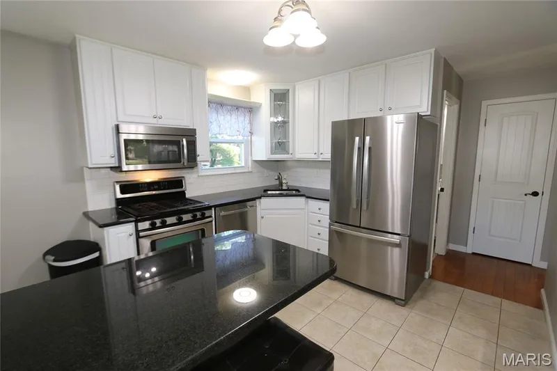 View from pantry. Kitchen featuring white cabinetry, black countertops, stainless steel appliances, and tile flooring — 3 Oxbow Road, St Peters, MO 63376