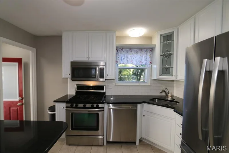 View from pass-through. White cabinetry with brushed nickel hardware, stainless steel appliances, dark countertops, a white subway tile backsplash, and ceramic tile flooring — 3 Oxbow Road, St Peters, MO 63376