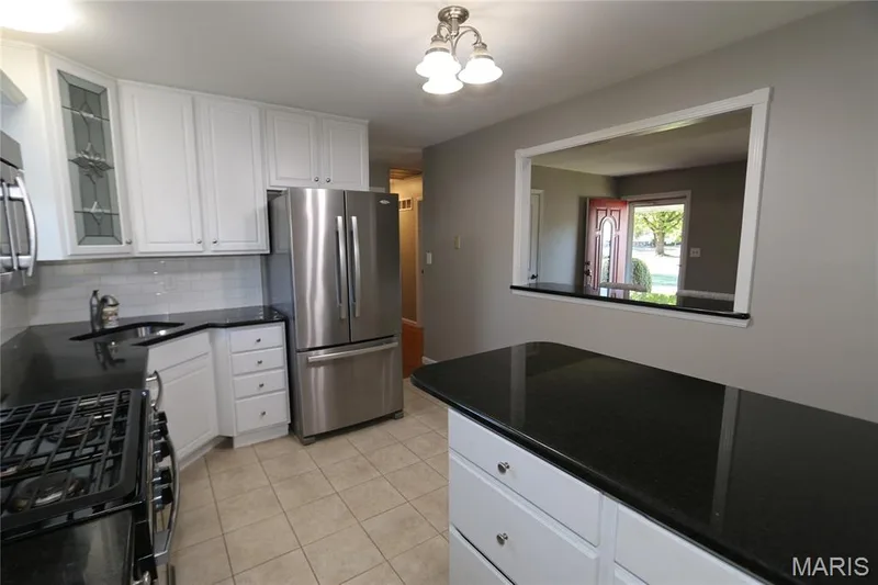 View from side door entrance. White cabinetry, black countertops, stainless steel appliances, tile flooring, and a kitchen island — 3 Oxbow Road, St Peters, MO 63376