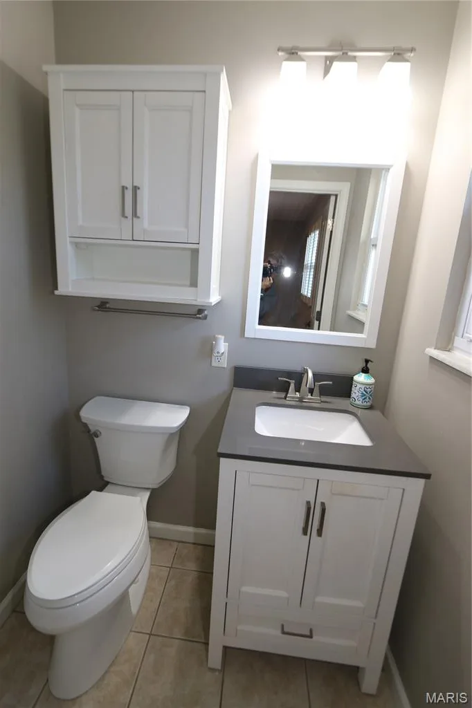 White vanity with a dark countertop and integrated sink, complemented by a white wall cabinet and mirror with overhead lighting — 3 Oxbow Road, St Peters, MO 63376