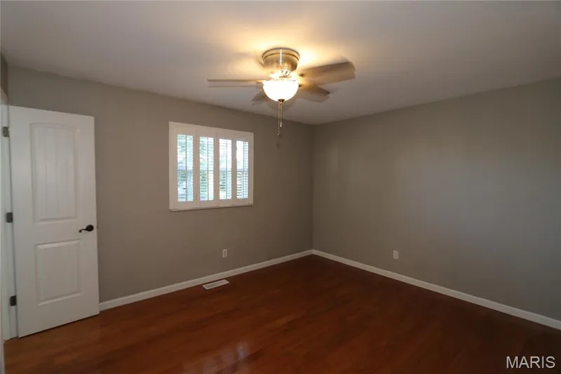 Shutters closed with slats open. Wood-finish flooring, plantation shutters, ceiling fan with integrated lighting, and a paneled interior door with matte black hardware — 3 Oxbow Road, St Peters, MO 63376