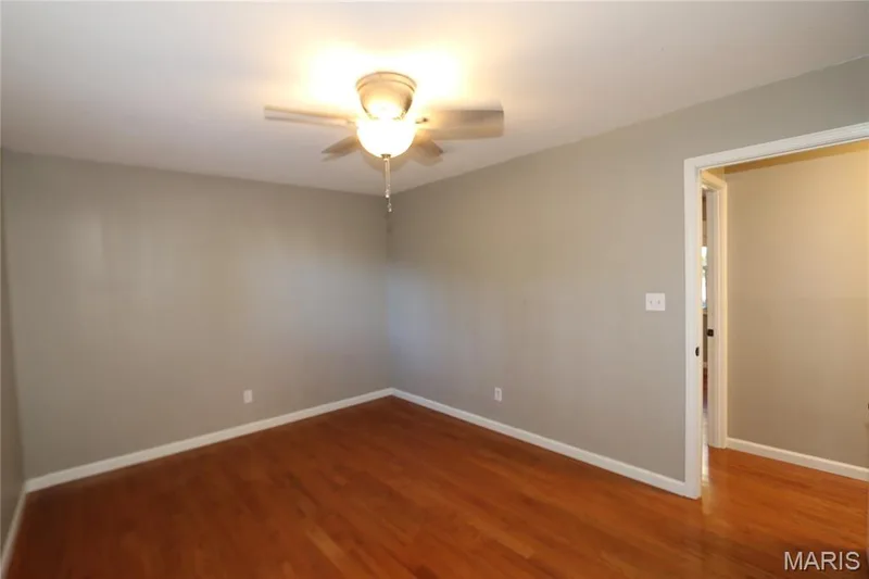 View of primary bedroom from primary bath doorway. Hardwood flooring, neutral wall paint, and a ceiling fan with integrated lighting — 3 Oxbow Road, St Peters, MO 63376