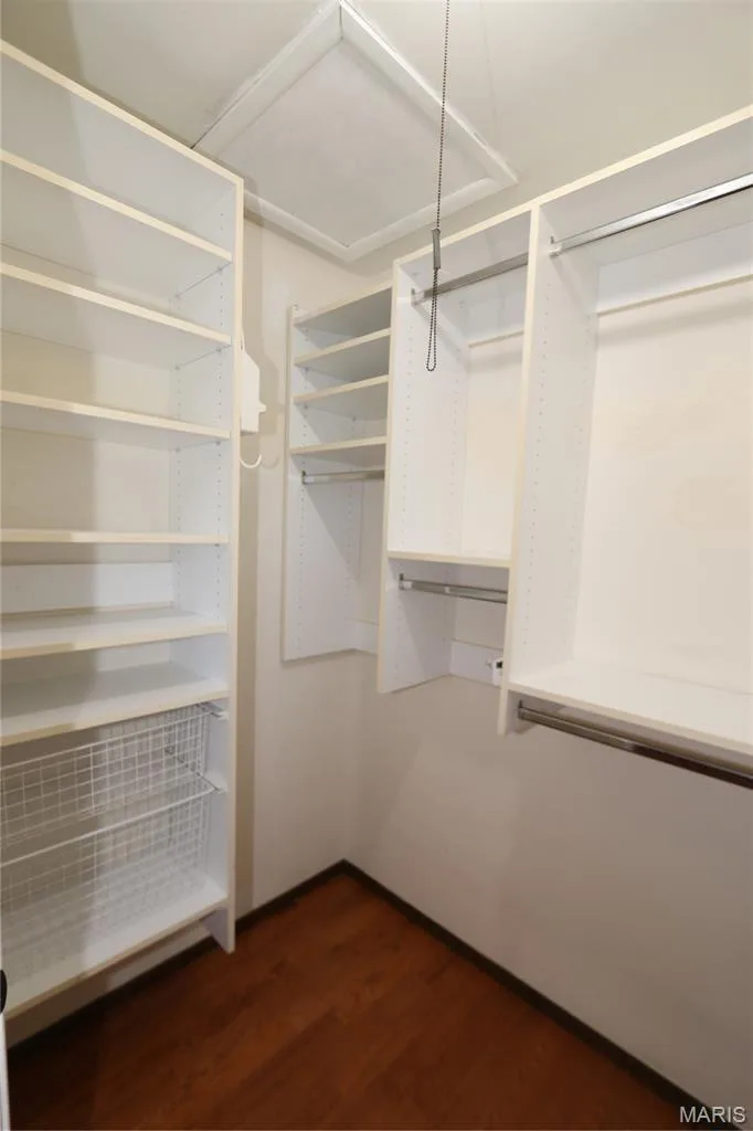 Primary Bedroom walk-in closet with organizer system. Walk-in closet featuring built-in white shelving, integrated hanging rods, a wire pull-out basket, and wood-finish flooring — 3 Oxbow Road, St Peters, MO 63376