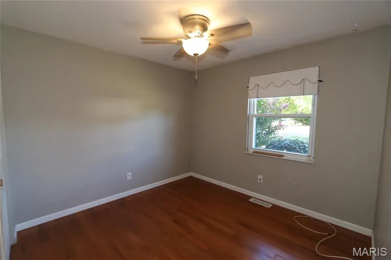 #2 Bedroom with pretty pink blooms just out the window. Hardwood-finish flooring, single window, overhead ceiling fan with light fixture, light gray wall paint, and white trim — 3 Oxbow Road, St Peters, MO 63376
