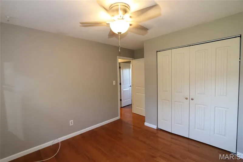 #2 Bedroom - View from back corner with door leading to hallway. Hardwood-style flooring, neutral wall tones, ceiling fan with integrated lighting, and bi-fold closet doors — 3 Oxbow Road, St Peters, MO 63376