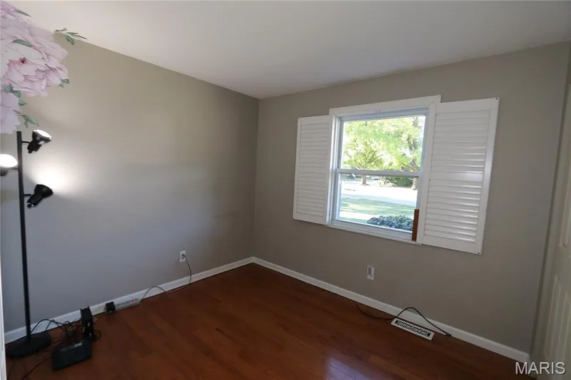 #3 Bedroom - View with shutters open to the sides. Hardwood flooring, painted walls, and a window with white louvered shutters — 3 Oxbow Road, St Peters, MO 63376