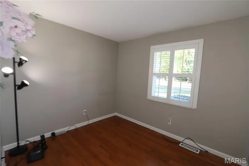 #3 Bedroom - view of room with shutters closed yet slats are open. Wood-finish flooring, neutral wall color, and window with white plantation shutters — 3 Oxbow Road, St Peters, MO 63376