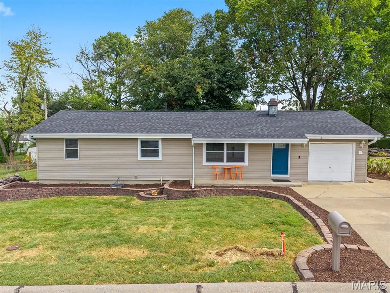 Beige vinyl siding with contrasting white trim, dark shingle roof, and a vibrant blue entry door — 712 Highland Drive, O'Fallon, MO 63366
