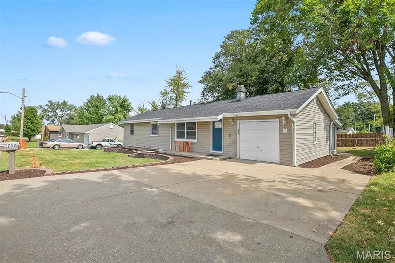 Single-story residence featuring light-colored siding, a dark shingle roof, an attached garage, and a concrete driveway — 712 Highland Drive, O'Fallon, MO 63366