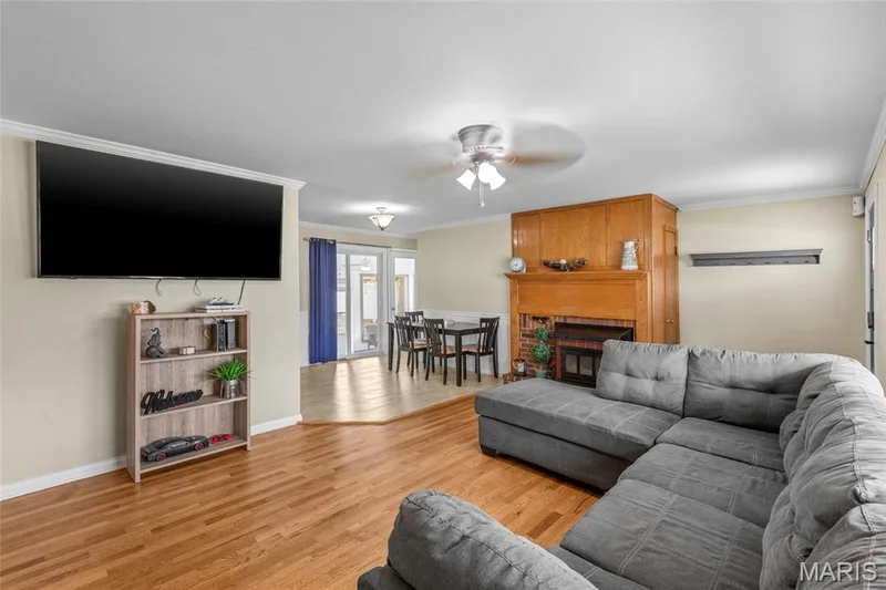 Hardwood flooring, wood-paneled fireplace surround, ceiling fan, crown molding, and sliding glass door — 712 Highland Drive, O'Fallon, MO 63366