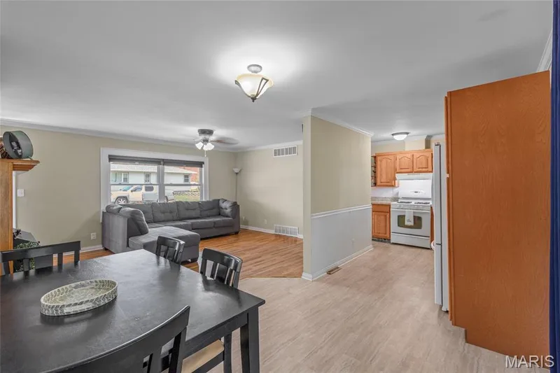 Wood-finish flooring in the living area, crown molding, a ceiling fan with integrated lighting, and a kitchen with wood cabinetry and tile-finish flooring — 712 Highland Drive, O'Fallon, MO 63366