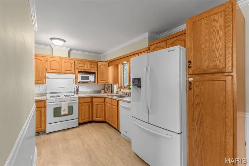 Kitchen featuring wood cabinetry, white appliances, light-toned countertops, and wood-finish flooring — 712 Highland Drive, O'Fallon, MO 63366