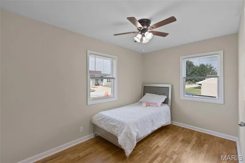 Hardwood-style flooring, neutral wall paint, two windows, and a ceiling fan with integrated lighting — 712 Highland Drive, O'Fallon, MO 63366