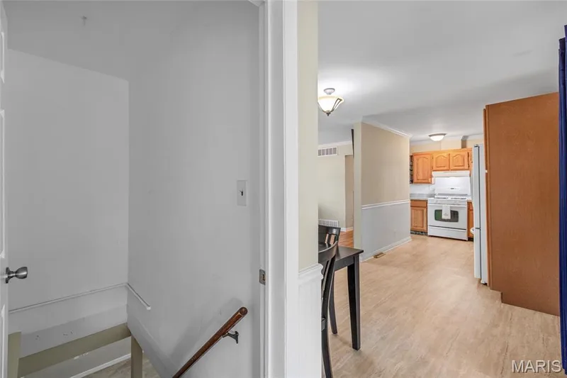 Kitchen featuring wood-finish flooring, wood cabinetry, white appliances, and a tile backsplash — 712 Highland Drive, O'Fallon, MO 63366