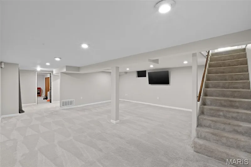 Expansive finished basement featuring recessed lighting, a carpeted staircase with a wood handrail, and soft gray carpeting — 712 Highland Drive, O'Fallon, MO 63366