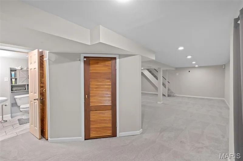 Recessed lighting, light gray carpeting, neutral wall color, wood louvered doors, and a partial bathroom with light tile flooring — 712 Highland Drive, O'Fallon, MO 63366