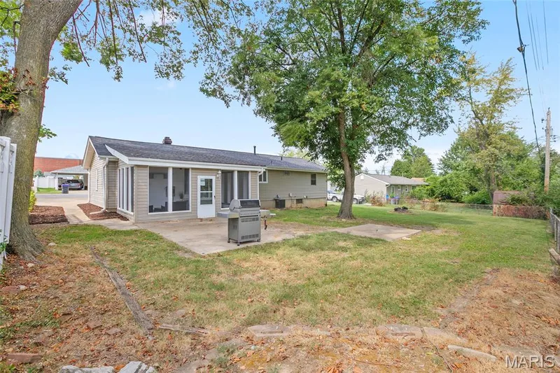 Expansive backyard featuring a concrete patio, mature trees, and a screened-in sunroom — 712 Highland Drive, O'Fallon, MO 63366